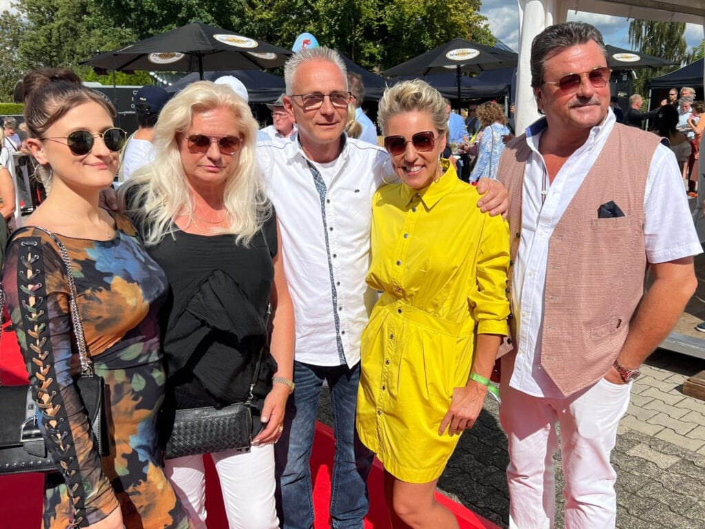 Gruppenfoto auf einem roten Teppich bei strahlendem Sonnenschein. Von links: Lena Reuer, ihre Mutter, Mitarbeiter Andreas Piasecki, die Künstlerin Alexandra Hoffmann (Aurelia Art, in gelbem Kleid) und Wilfried Reuer. Alle lächeln in die Kamera.